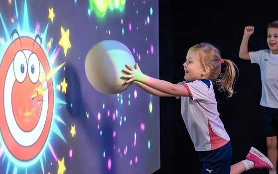 Kleines Mädchen wirft einen großen Softball an die Spielwand
